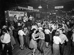 Crowded 1960s Bakersfield dance hall with people dancing to a live country band.